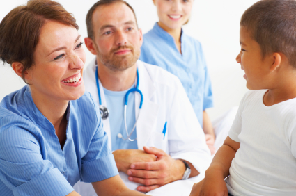 A smiling nurse and doctor talk with a young patient in a clinical setting.