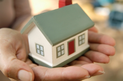 Small model house cradled in cupped hands, symbolizing care for home.